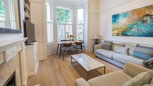A living room with a fireplace, a dining table with chairs, a sofa, and a large abstract painting on the wall. - Charming 3-Bed Haven in Little Venice with a Private Outdoor Oasis (London)
