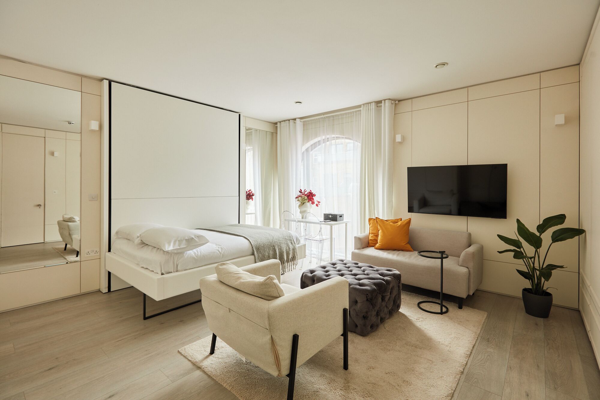 Ein modernes Schlafzimmer mit Bett, Sofa, Fernseher und einer Zimmerpflanze.