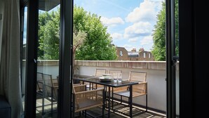 A balcony with a glass table and wicker chairs, overlooking a residential area with trees and houses. - Loftus Road (London)