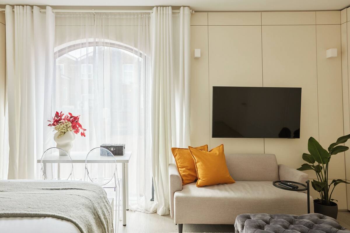 A modern bedroom with a bed, a sofa, a TV, a table with a vase of flowers, and a potted plant.