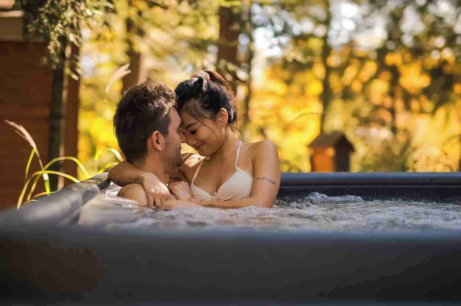 A couple in a hot tub surrounded by trees.