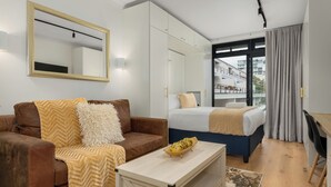 A modern hotel room with a sofa, a bed, a desk, and a large window. - The Sage | Cosy Studio in Vibrant Sea Point | Netflix | WIFI (Cape Town)