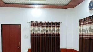 Una habitación con techo de madera, un reloj en la pared, una ventana con cortinas y un banco con cajones.