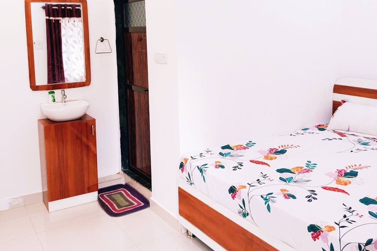 Una camera da letto con un letto, un comodino in legno, un lavandino bianco, uno specchio e una ventola a soffitto.