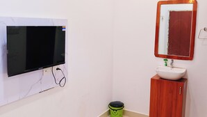 Un baño con un televisor montado en la pared, un lavabo con un espejo encima y un cubo de basura verde.