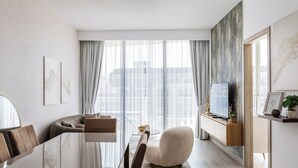 A modern living room with a glass dining table, a sofa, and a TV on a wooden stand.