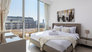 A modern hotel room with a large bed, a desk, and a view of the cityscape.
