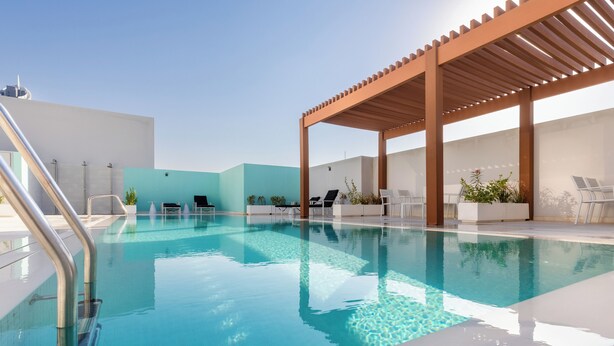 A swimming pool with a wooden pergola, lounge chairs, and potted plants.