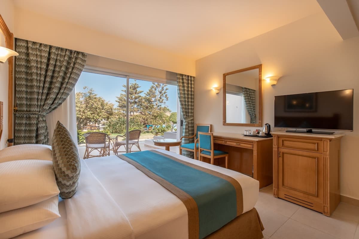 A hotel room with a large bed, a desk with a chair, a television, and a view of the outdoors.
