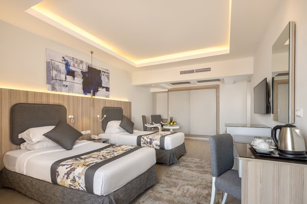 A modern hotel room with two beds, a desk, and a television.