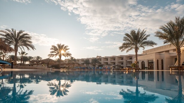 A resort pool with palm trees and a building in the background. - Hurghada Long Beach Resort (Hurghada)