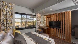 A modern hotel room with a large bed, a TV mounted on a wooden panel, and a view of the outdoors through a large window. - Hurghada Long Beach Resort (Hurghada)