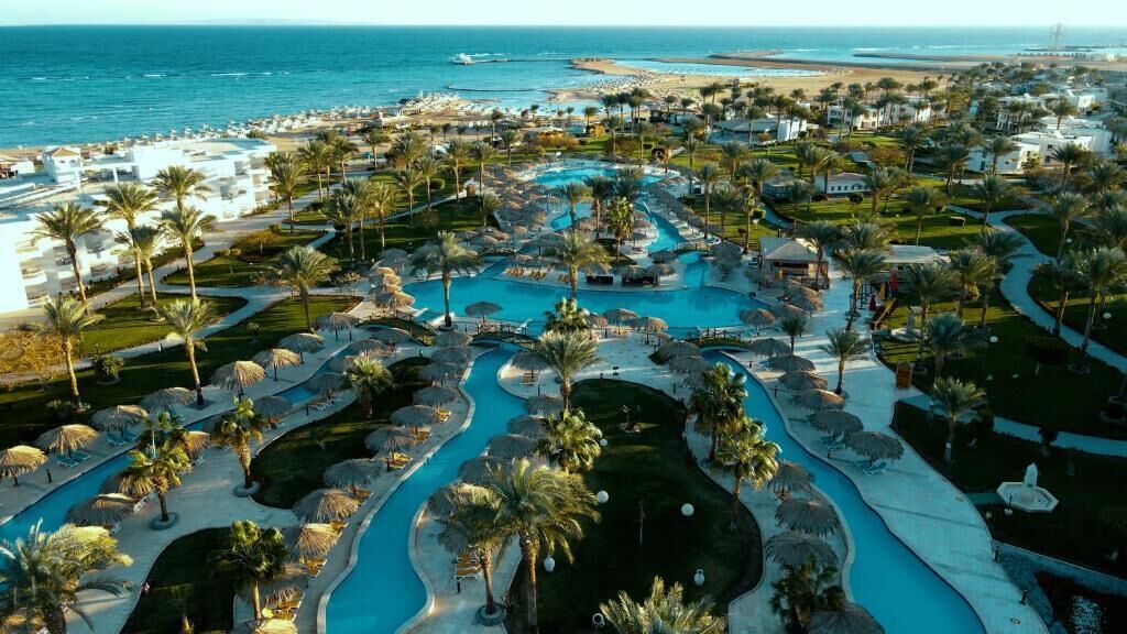 A resort with a large swimming pool, palm trees, and a view of the beach.
