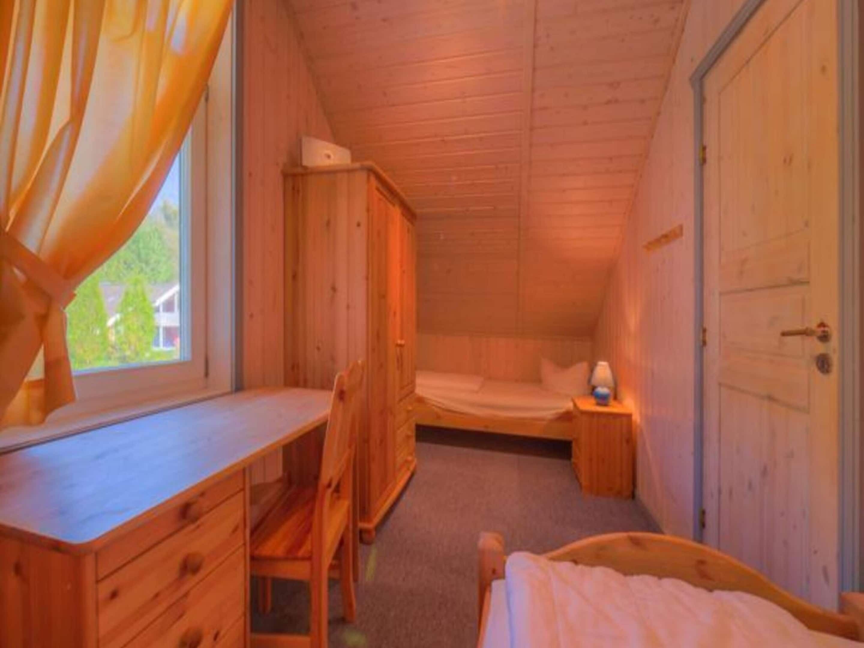 A wooden cabin bedroom with a desk, a bed, and a nightstand.