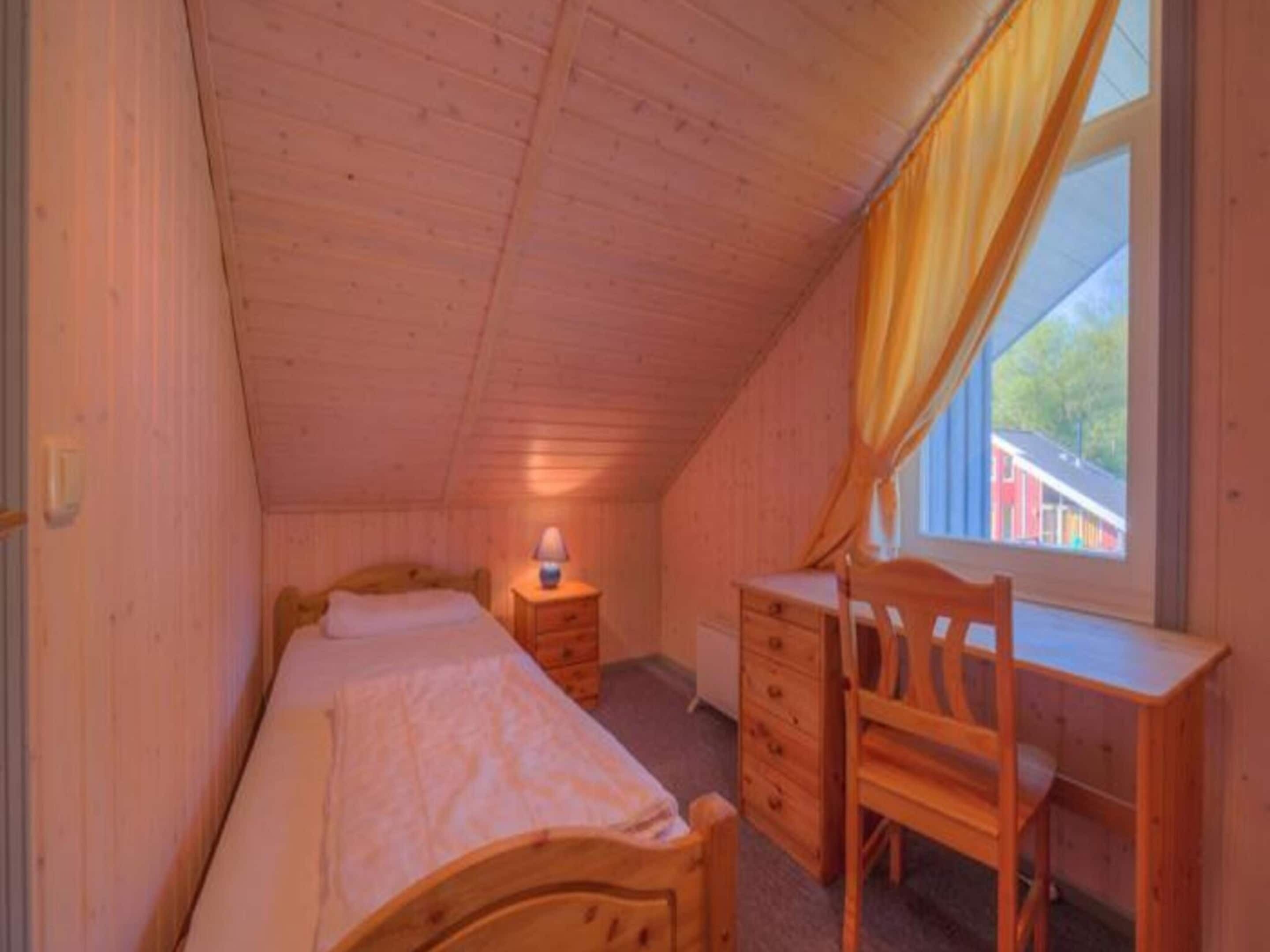 Una stanza piccola e accogliente con un letto singolo, una scrivania in legno e una finestra con tende.