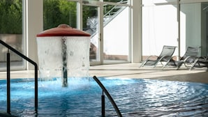 Una piscina con elemento d'acqua, poltrone relax e ampie finestre.