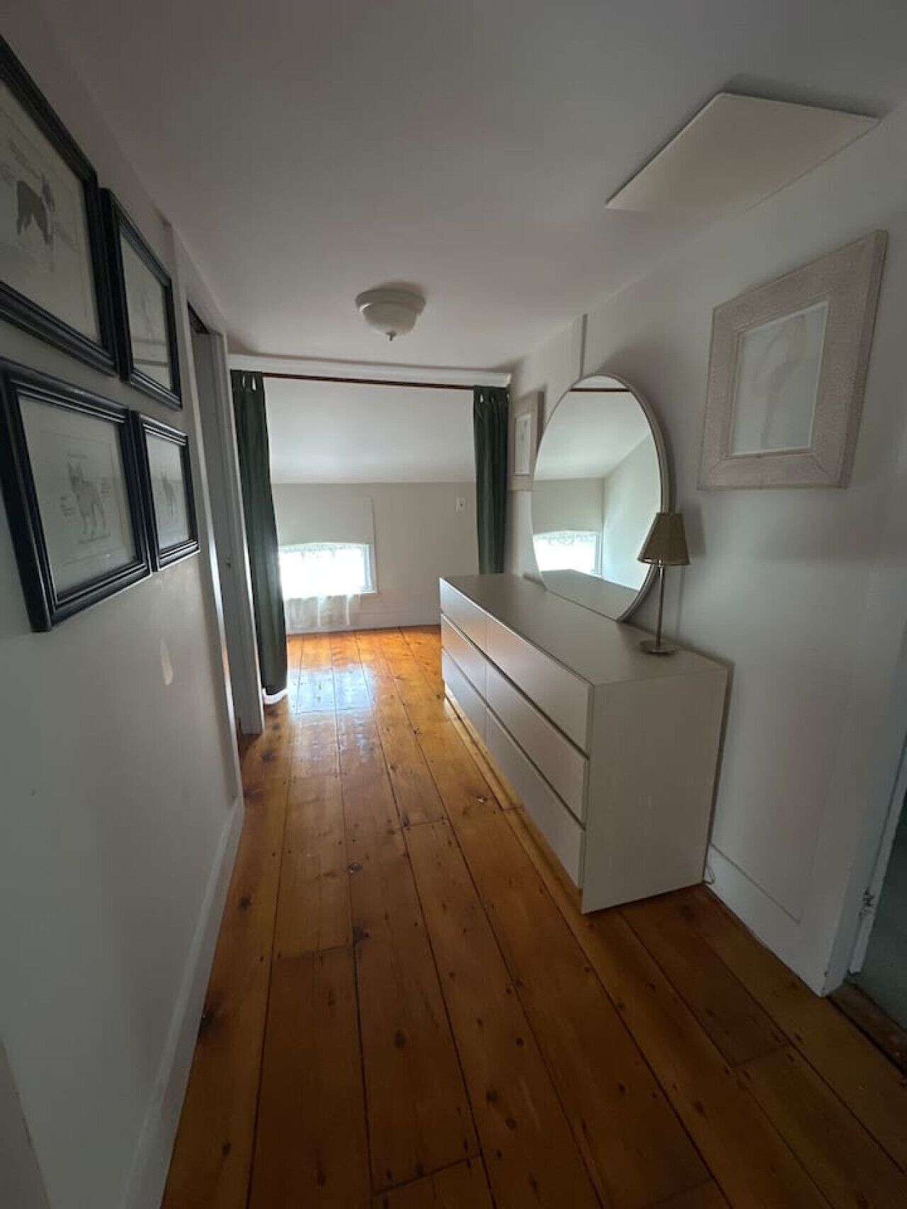 A room with a wooden floor, a white dresser, a mirror, and framed pictures on the wall.
