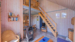 A cozy room with a wooden staircase, a fireplace, a bookshelf, and a dining area. - Ferienhaus im Skandinavischen Stil (Rechlin)