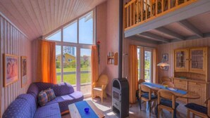 A cozy room with a sofa, a table, a grill, and a dining area with chairs and a cabinet. - Ferienhaus im Skandinavischen Stil (Rechlin)