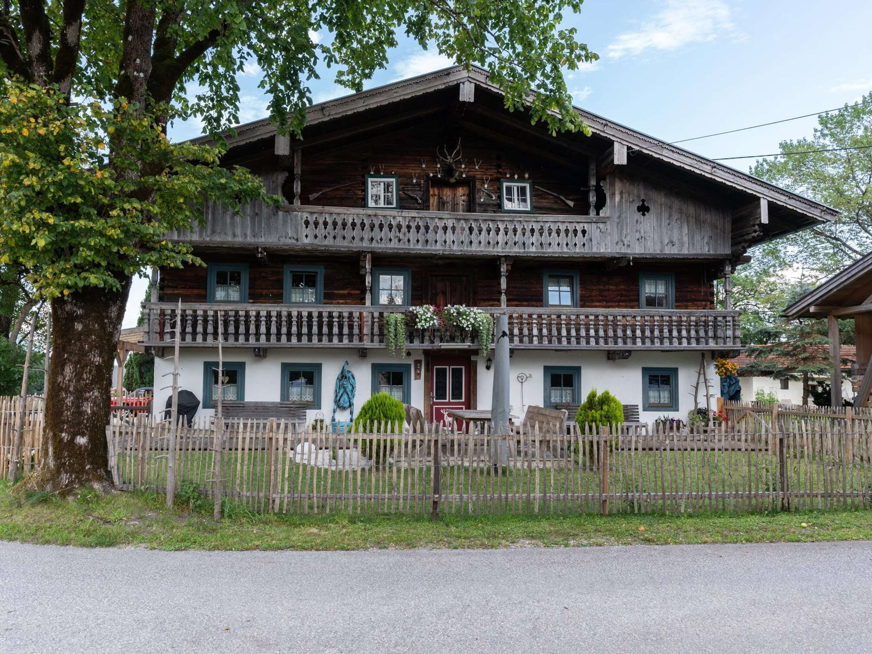 A traditional wooden building with a balcony, a fence, and a tree in front.