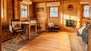 Un chalet confortable avec un intérieur en bois, un coin repas avec des chaises et une table, et un lit recouvert d’une couverture à motifs.