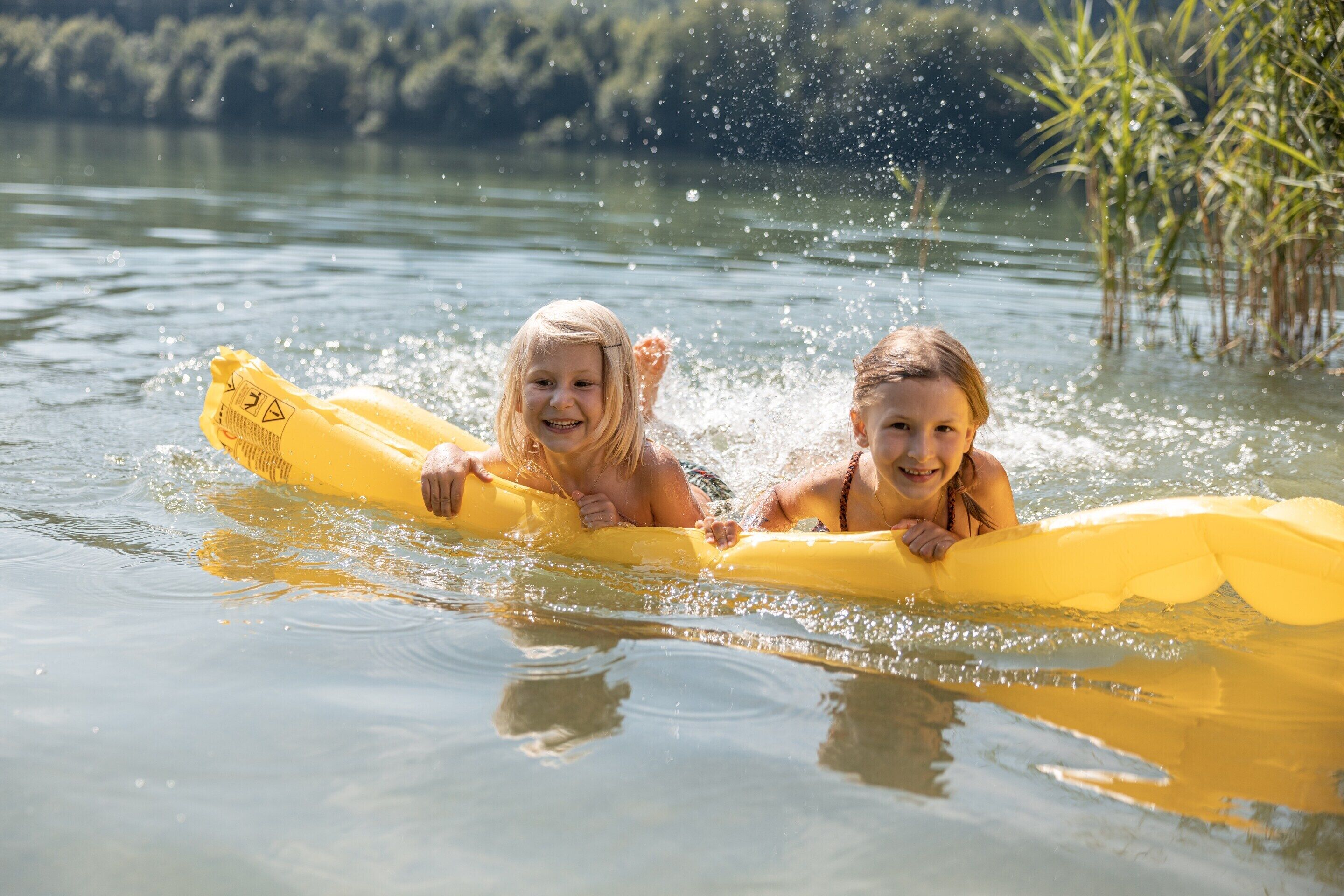 Two individuals on a yellow raft in a body of water with vegetation in the background.