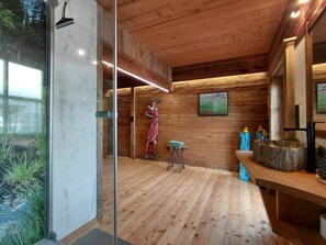 L’intérieur d’une cabane en bois, avec une porte en verre, un plancher en bois, une petite table recouverte d’une nappe bleue et un tableau accroché au mur.
