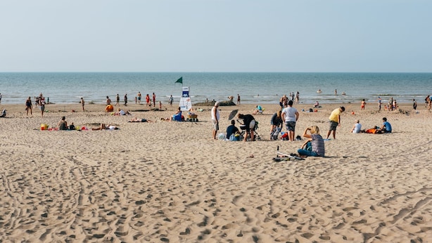 Una playa arenosa con gente tomando el sol y nadando.