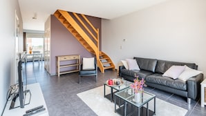 Una sala de estar moderna con una escalera, un sofá, una mesa de centro y un televisor.