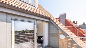 Un balcón moderno con puerta corrediza de vidrio, piso de madera y barandilla de metal.