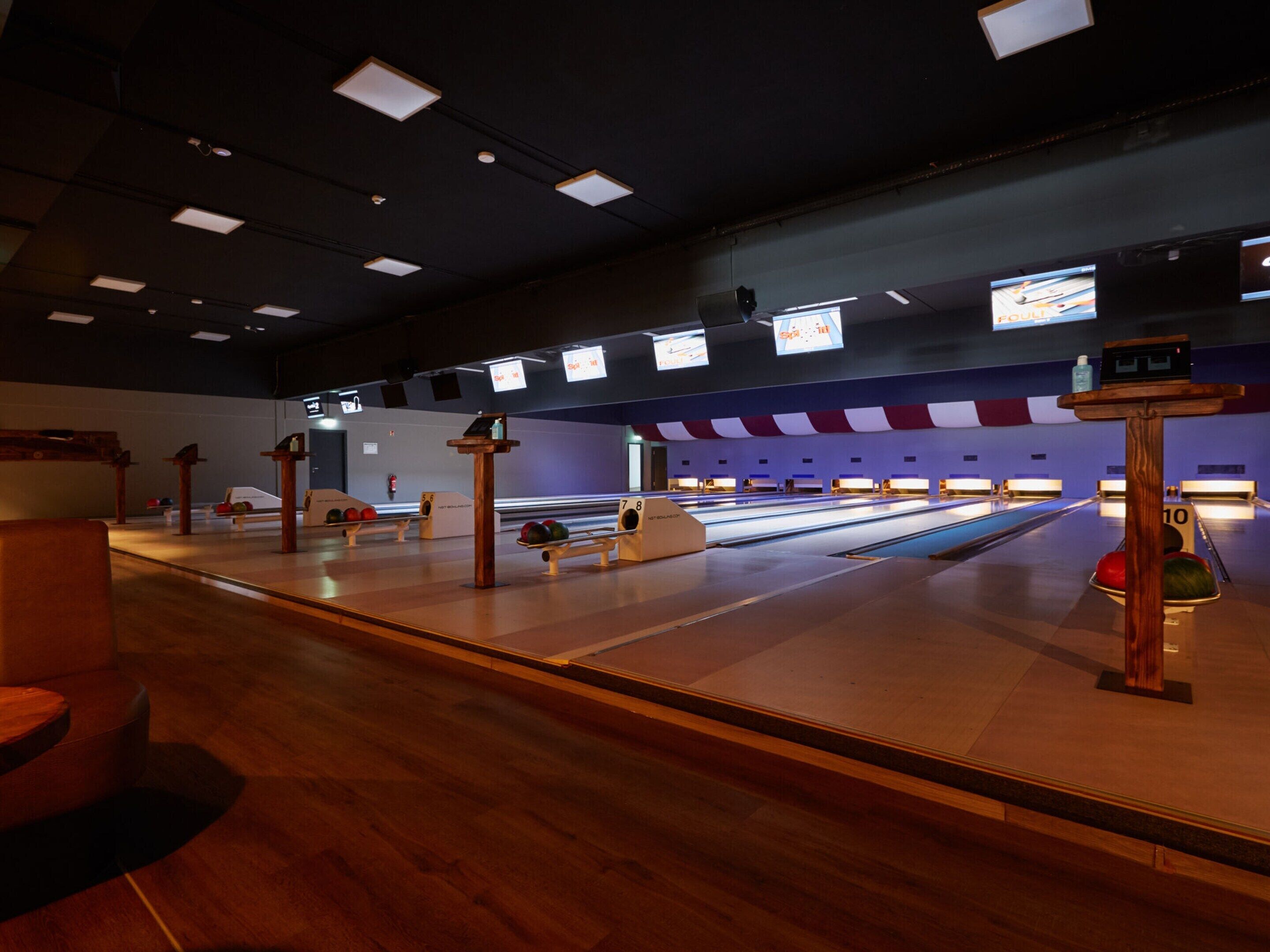 A bowling alley with multiple lanes, wooden furniture, and overhead lighting.