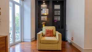 Una habitación acogedora con un sillón beige, una puerta negra decorada con marcos de fotos y un ventanal con vistas al balcón.