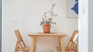 Una pequeña mesa de madera con una maceta de terracota que contiene una planta, flanqueada por dos sillas de mimbre.