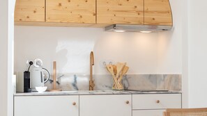 A modern kitchen with wooden cabinets, a marble countertop, a coffee maker, a kettle, and wooden utensils.