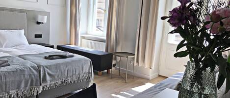 A modern hotel room with a neatly made bed, a small table with a vase of flowers, and a window with curtains.