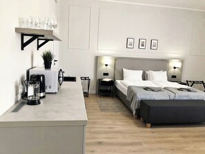 Camera d'albergo moderna con un letto, comodini, una macchina del caffè, un tavolino con dei bicchieri e una pianta.