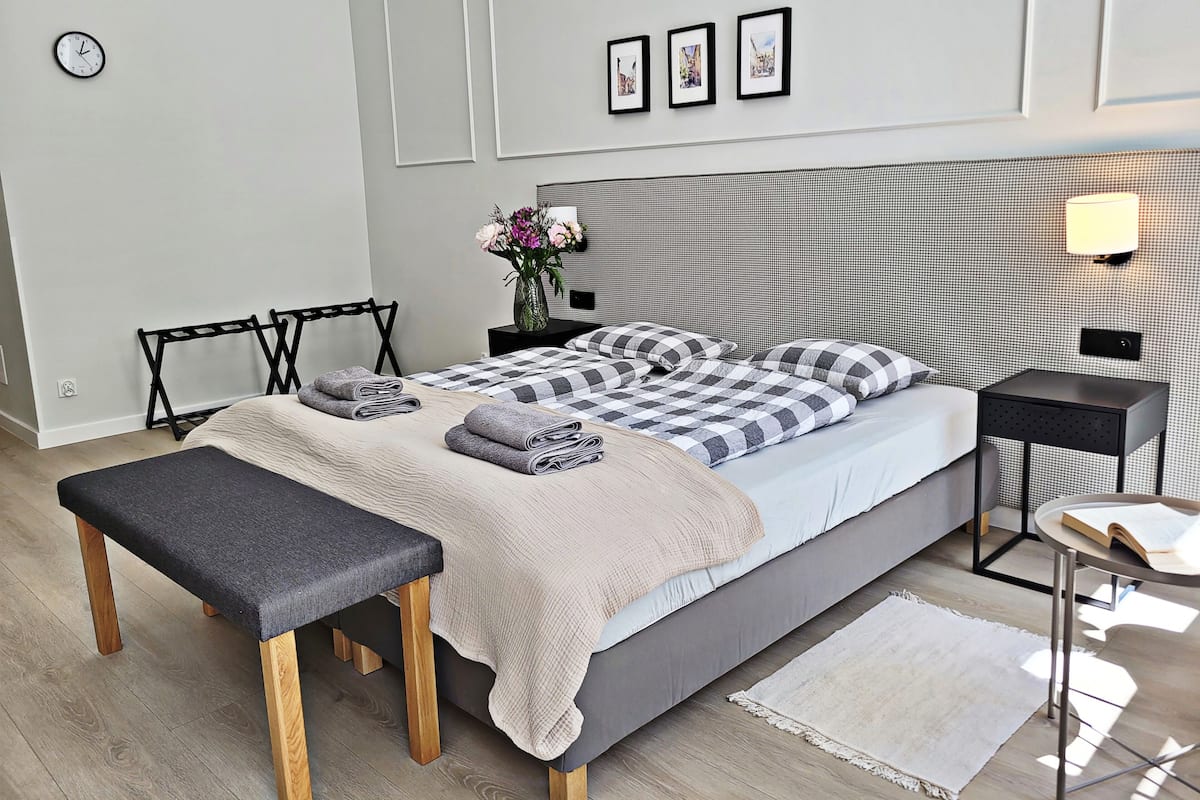 Quarto moderno com cama, banqueta, mesa de cabeceira e luminária na parede.