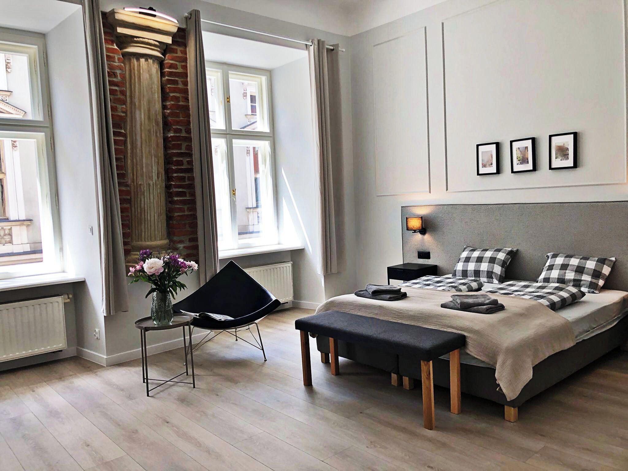 Un dormitorio moderno con una cama grande, una silla negra, un banco y un ventanal con cortinas.