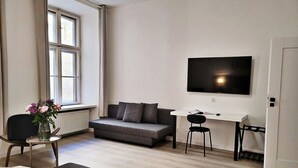 A modern living room with a sofa, a small table with a vase of flowers, a TV mounted on the wall, and a wooden floor. - Anny 5 Apartamenty (Kraków)