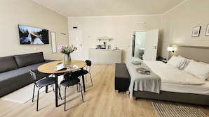 A modern hotel room with a bed, a sofa, a dining table with chairs, a small kitchen area, and a TV mounted on the wall. - Anny 5 Apartamenty (Kraków)