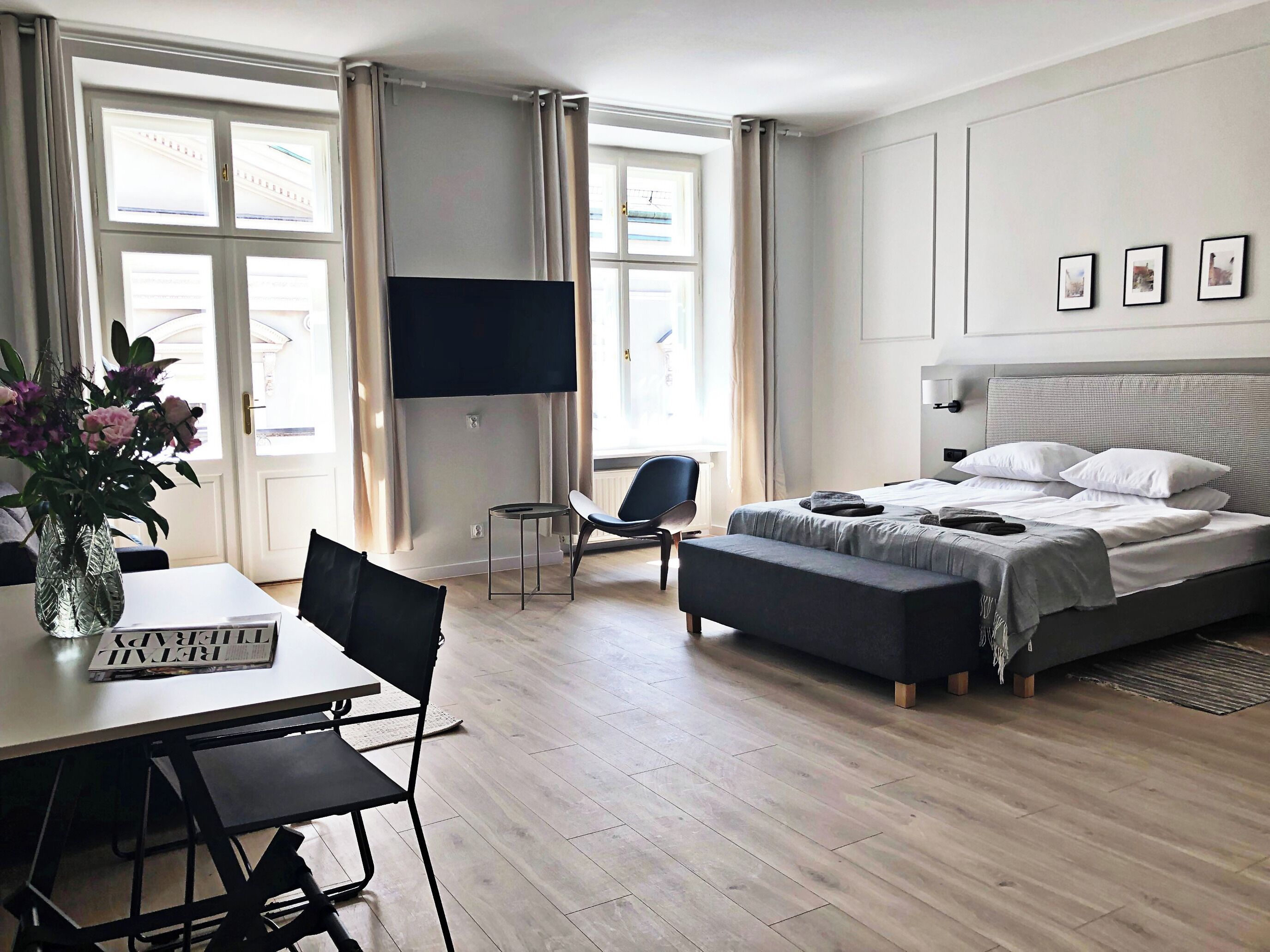 A modern hotel room with a bed, a desk with a chair, a TV, and a window with curtains.