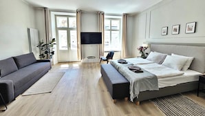 A modern hotel room with a large bed, a sofa, a TV, and a view of the city through large windows. - Anny 5 Apartamenty (Kraków)