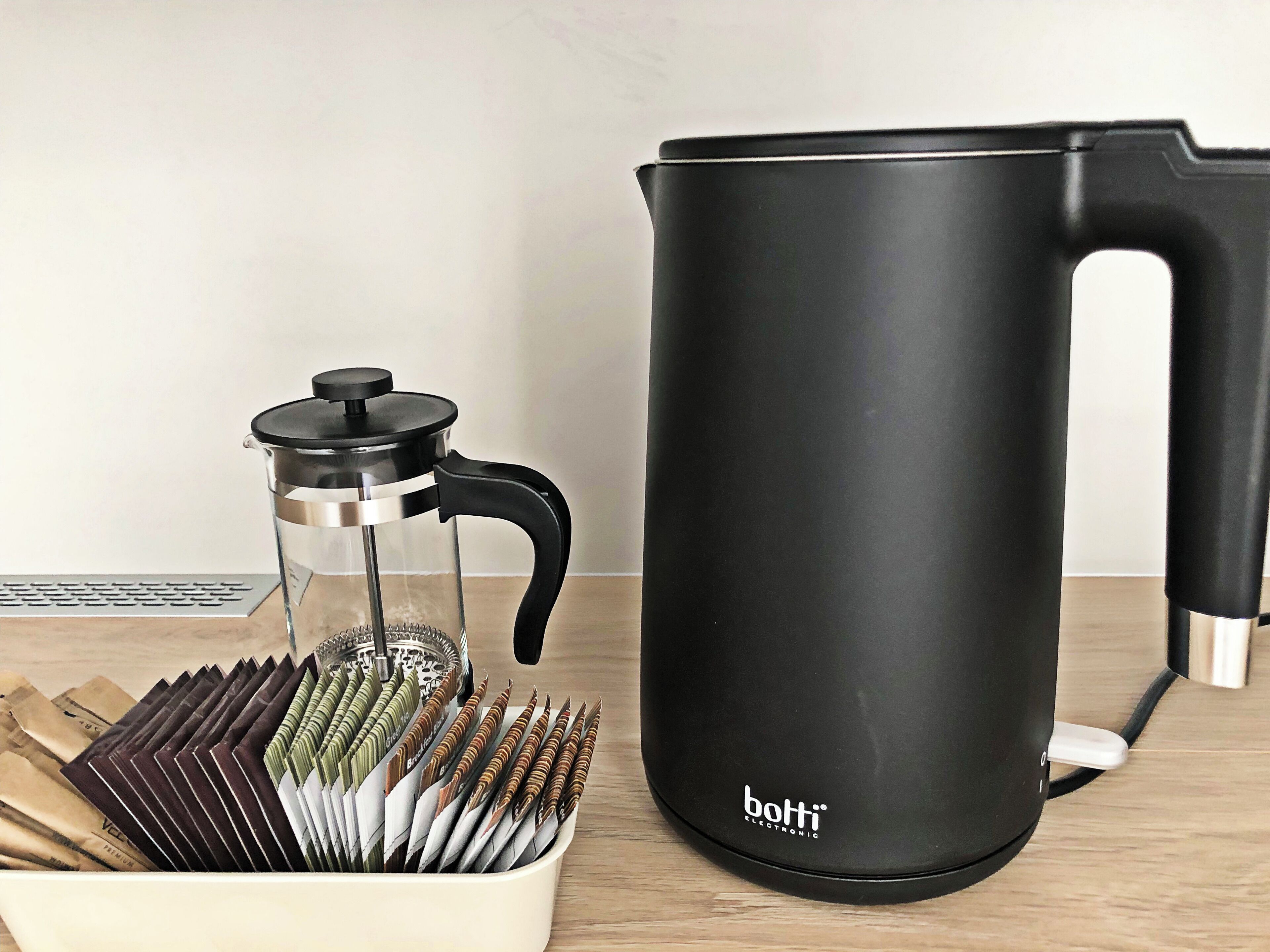 A black electric kettle and a French press coffee maker on a wooden table.