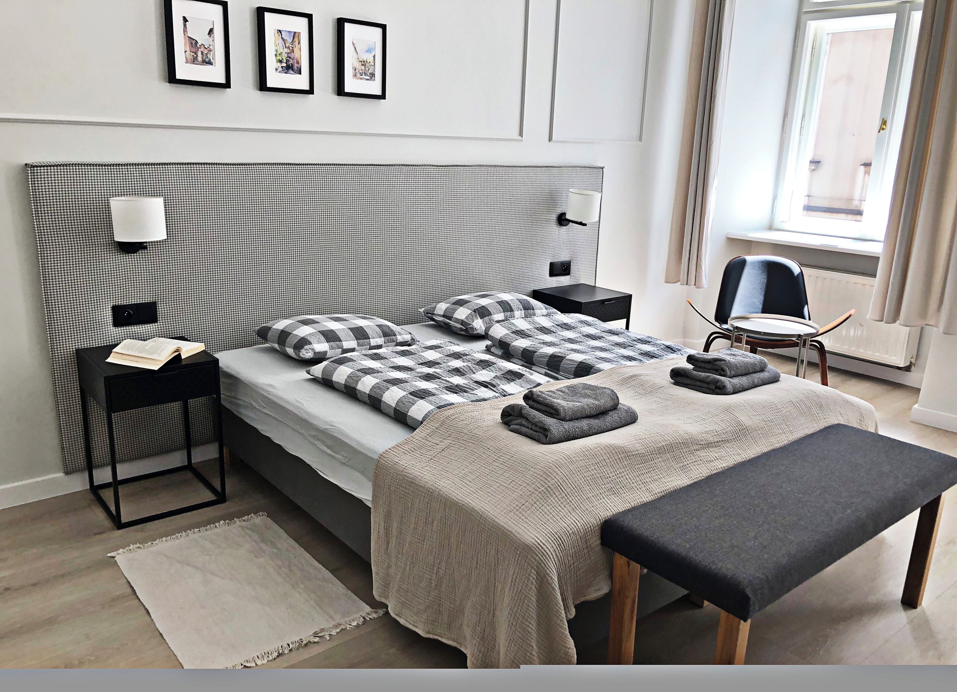 Un dormitorio moderno con una cabecera de cuadros, una mesita de noche con lámpara, un banco y vistas al exterior.