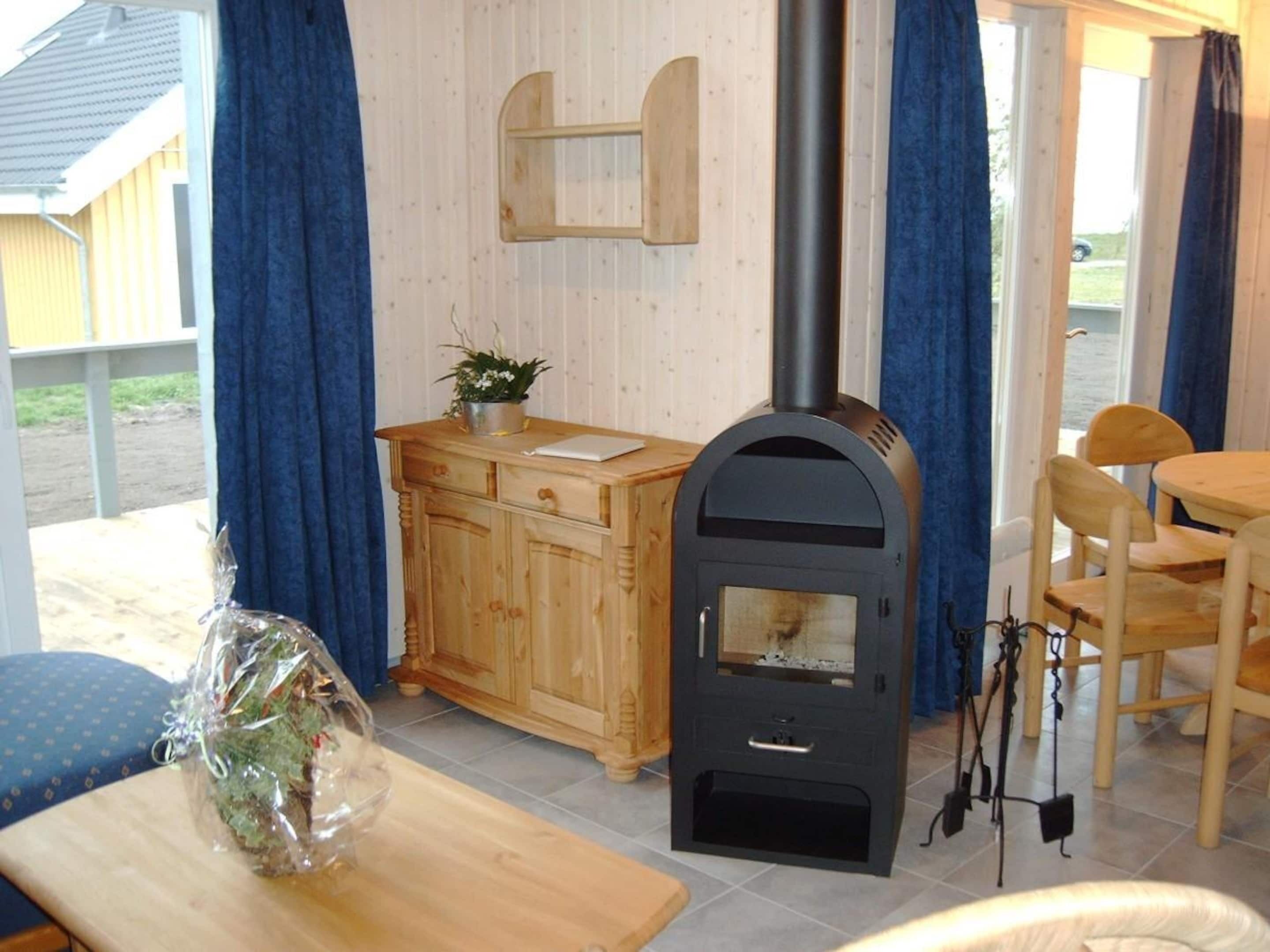 Une pièce chaleureuse avec un meuble en bois, une table agrémentée d’une plante, un poêle en bois noir et un coin repas avec des chaises.