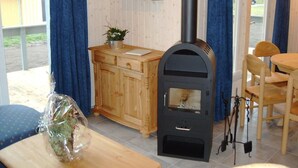 A cozy room with a wooden cabinet, a table with a wrapped item, a black wood stove, and a chair. - Ferienhaus im Skandinavischen Stil (Rechlin)