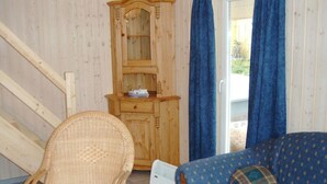 A room with a wicker chair, a blue patterned sofa, a wooden cabinet with a mirror, and a sliding glass door with blue curtains. - Ferienhaus im Skandinavischen Stil (Rechlin)