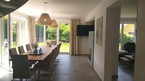 Ein zeitgemäßer Essbereich mit einem langen Tisch, Stühlen und einer großen, gewebten Leuchte.