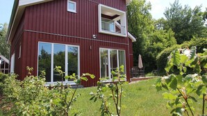 Ein zweigeschossiges Haus mit roter Fassade, großen Schiebeglastüren und einem Balkon im oberen Stockwerk.