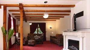 A cozy living room with a fireplace, wooden beams, a television, and a red carpet. - Ferienhaus Monika in Wendorf im Bernstein Resort (Kuhlen-Wendorf)